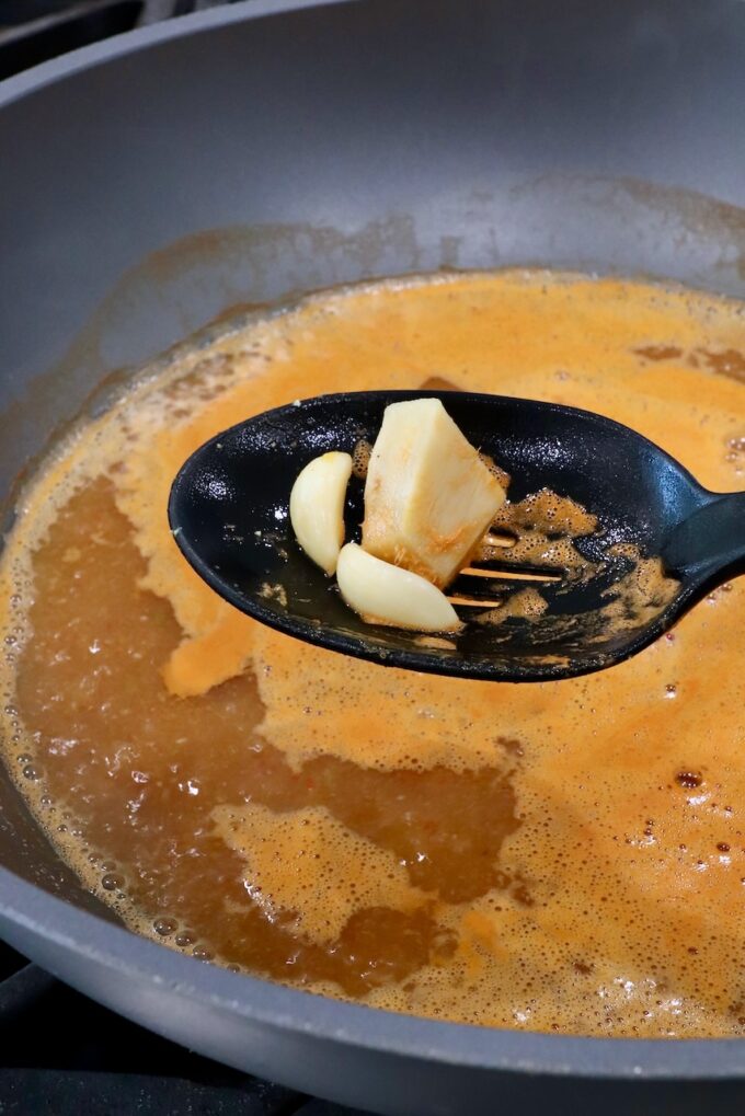 garlic cloves and ginger in a slotted spoon held above a pot of broth