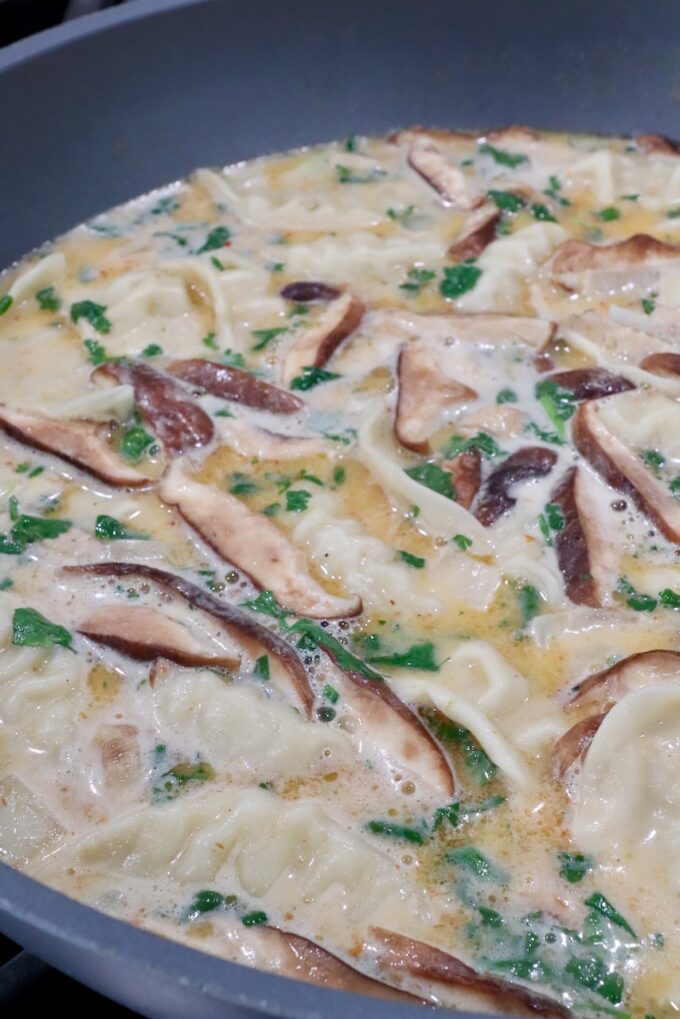 cilantro, mushrooms and potstickers in a pot of creamy coconut broth