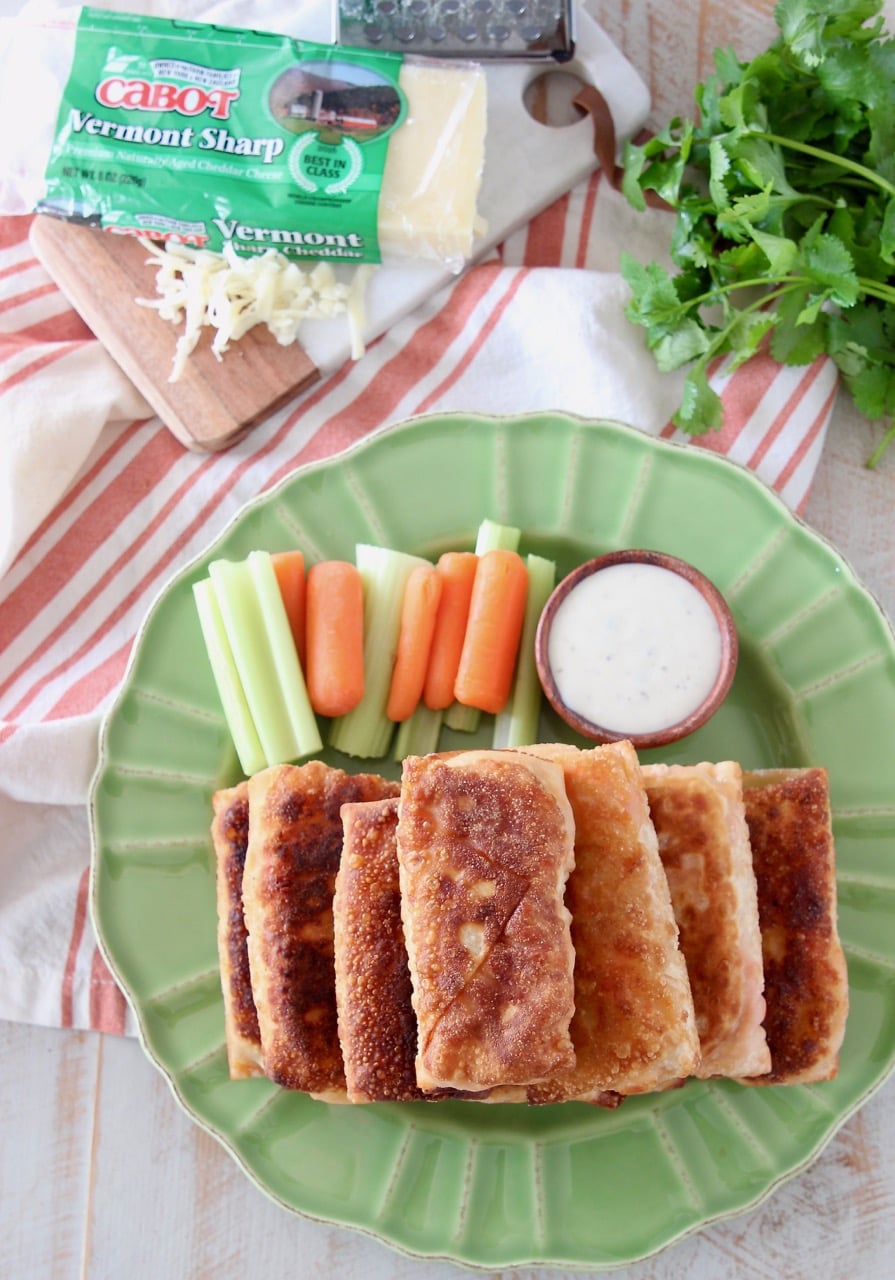 Overhead shot of buffalo chicken egg rolls stacked on top of each other on a green plate with carrot and celery sticks and a wood ramekin of ranch dressing