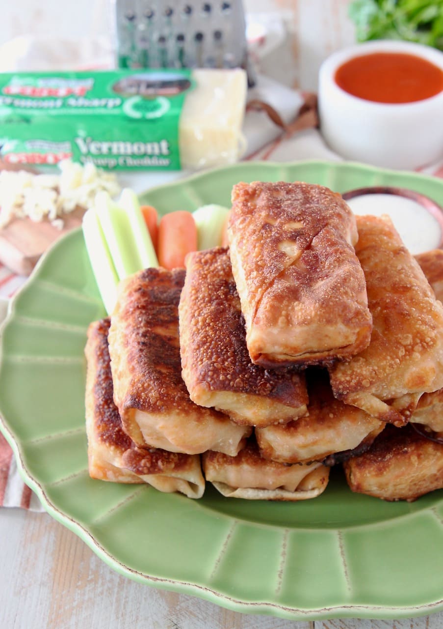 Buffalo chicken egg rolls piled up on top of green plate with carrot sticks and celery sticks in the background