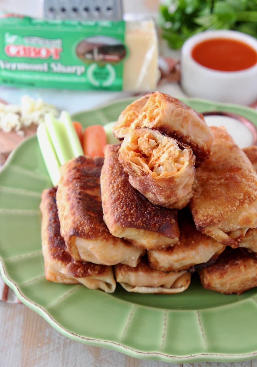 Buffalo chicken egg rolls stacked on each other on a green plate with the top egg roll cut in half