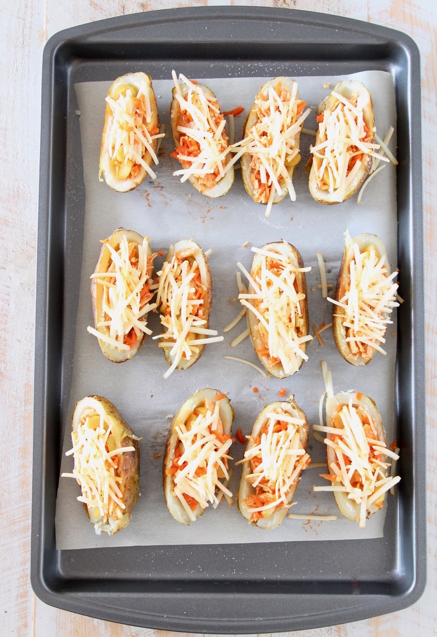 Potato skins filled with buffalo chicken and shredded cheddar cheese on baking sheet