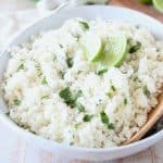 Cilantro lime rice in large white bowl with wooden spoon and lime wedges on top