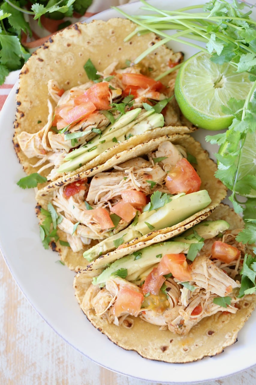 Shredded pressure cooker chicken tacos in corn tortillas on white plate with cilantro and lime