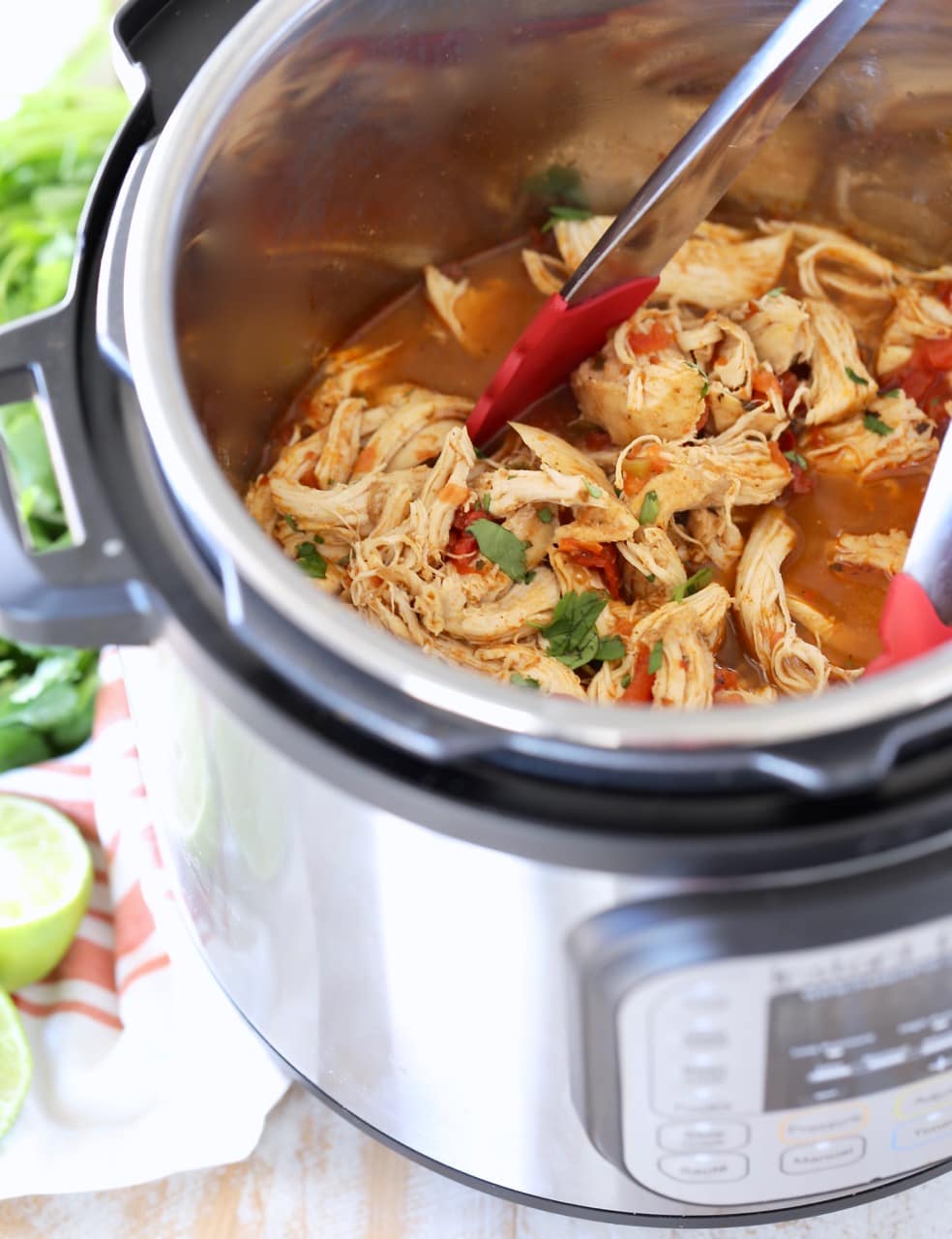 Shredded taco chicken in Instant Pot with red tongs and cilantro