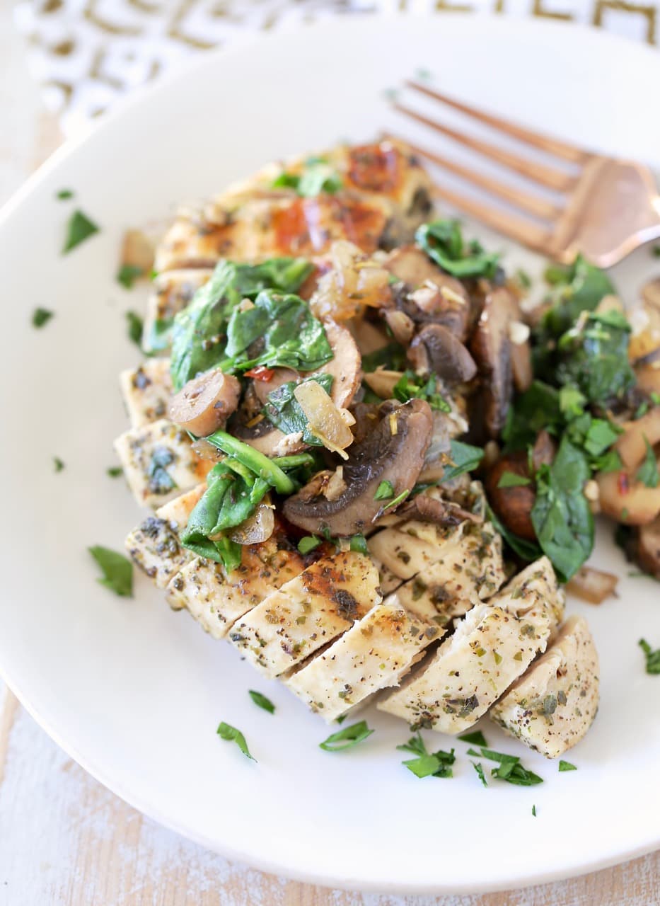 Grilled sliced chicken on plate, topped with sauteed mushrooms and spinach with copper fork on side of plate, garnished with fresh chopped parsley