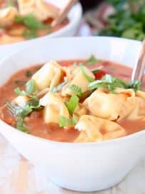 Tortellini soup in white bowls with copper spoons and fresh parsley