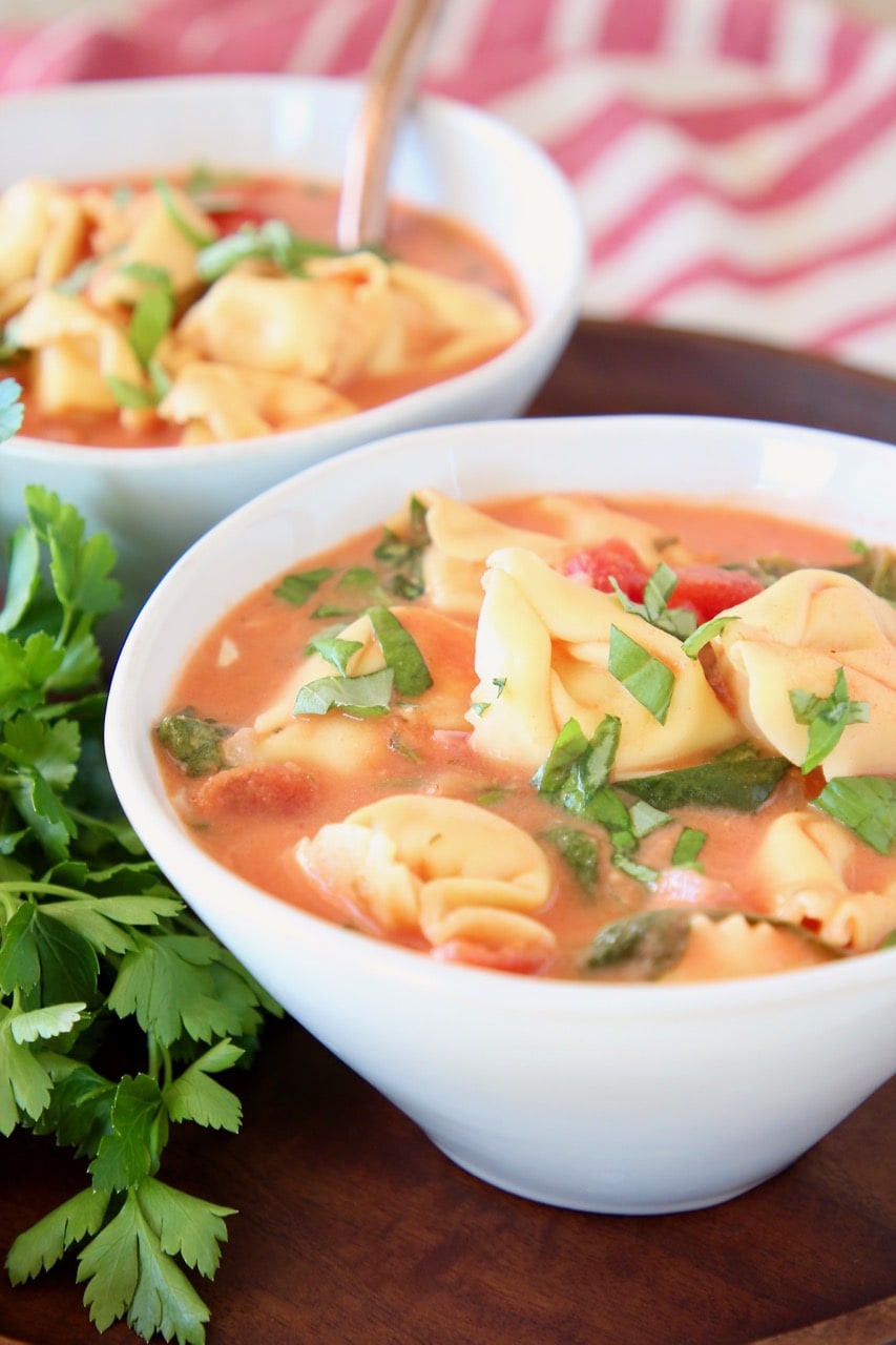 Creamy tomato tortellini soup in white bowl with fresh parsley and diced tomatoes