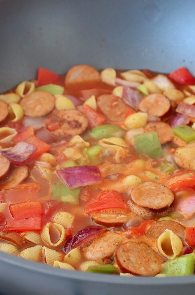 sliced sausage, peppers, onions and pasta shells in a tomato broth in a large skillet