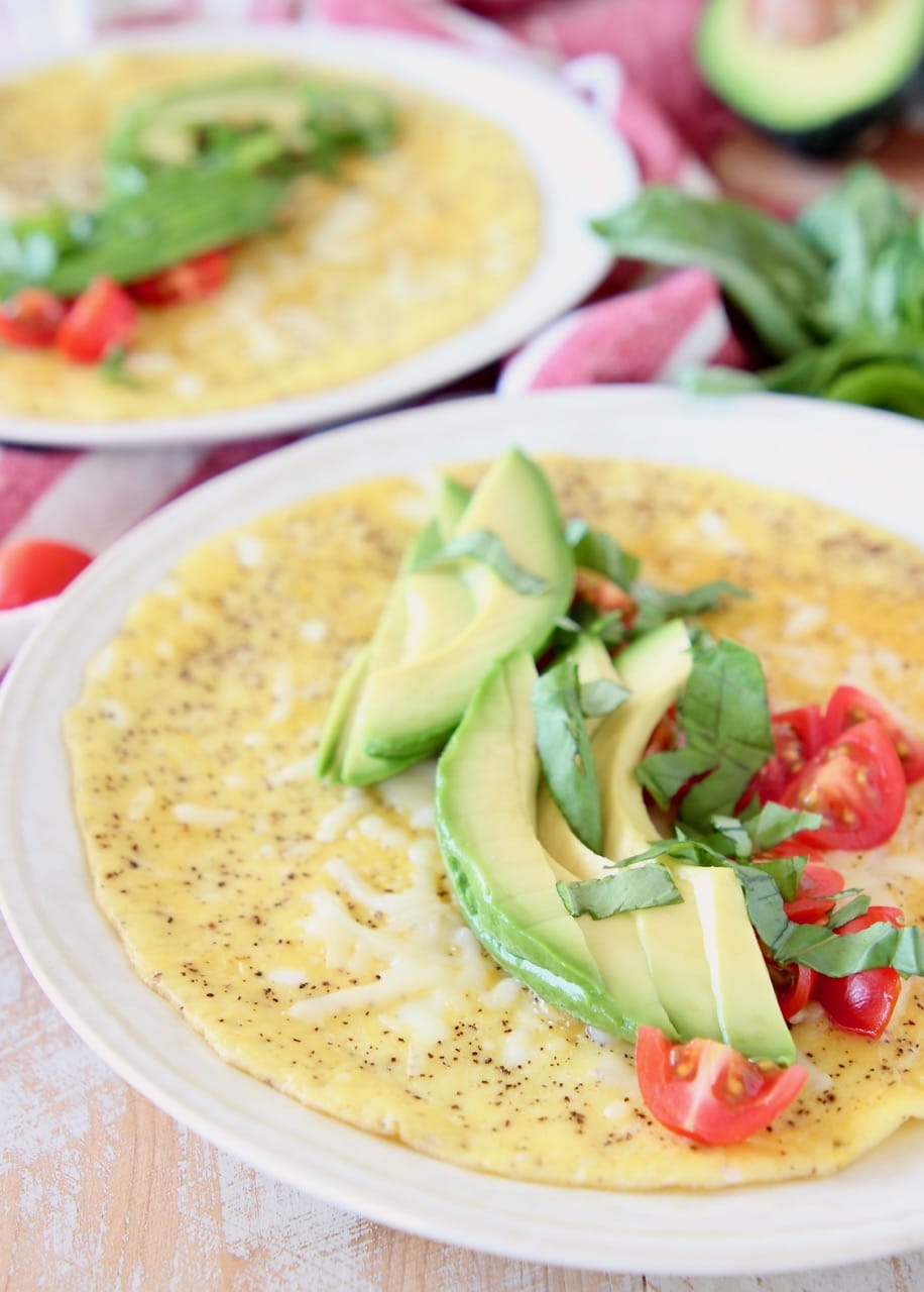 Avocado omelette with diced tomatoes and fresh basil on white plate