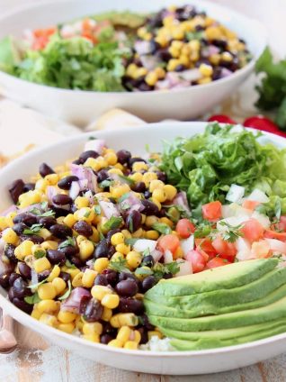 White bowl with sliced avocado, black bean and corn relish, diced tomatoes and shredded lettuce