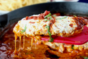 Chicken parmesan on a spatula coming out of a large cast iron skillet