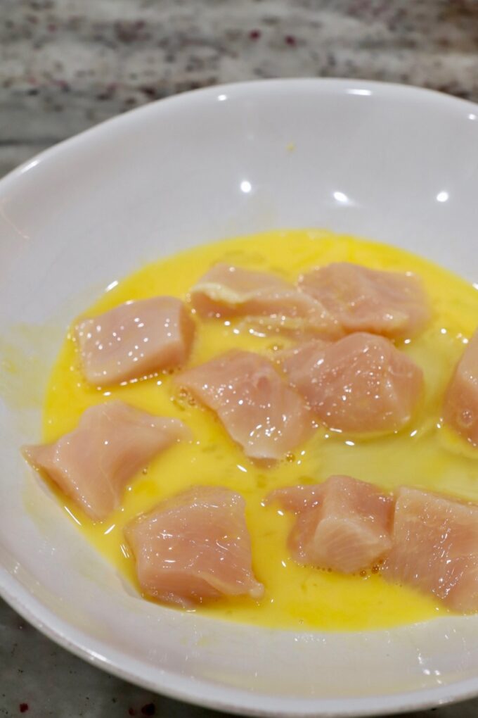 pieces of chicken dipped in a whisked egg in a bowl