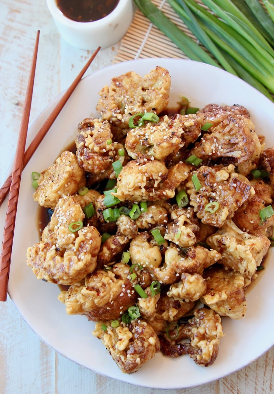 Fried Cauliflower piled up on white plate topped with Korean BBQ Sauce and diced green onions