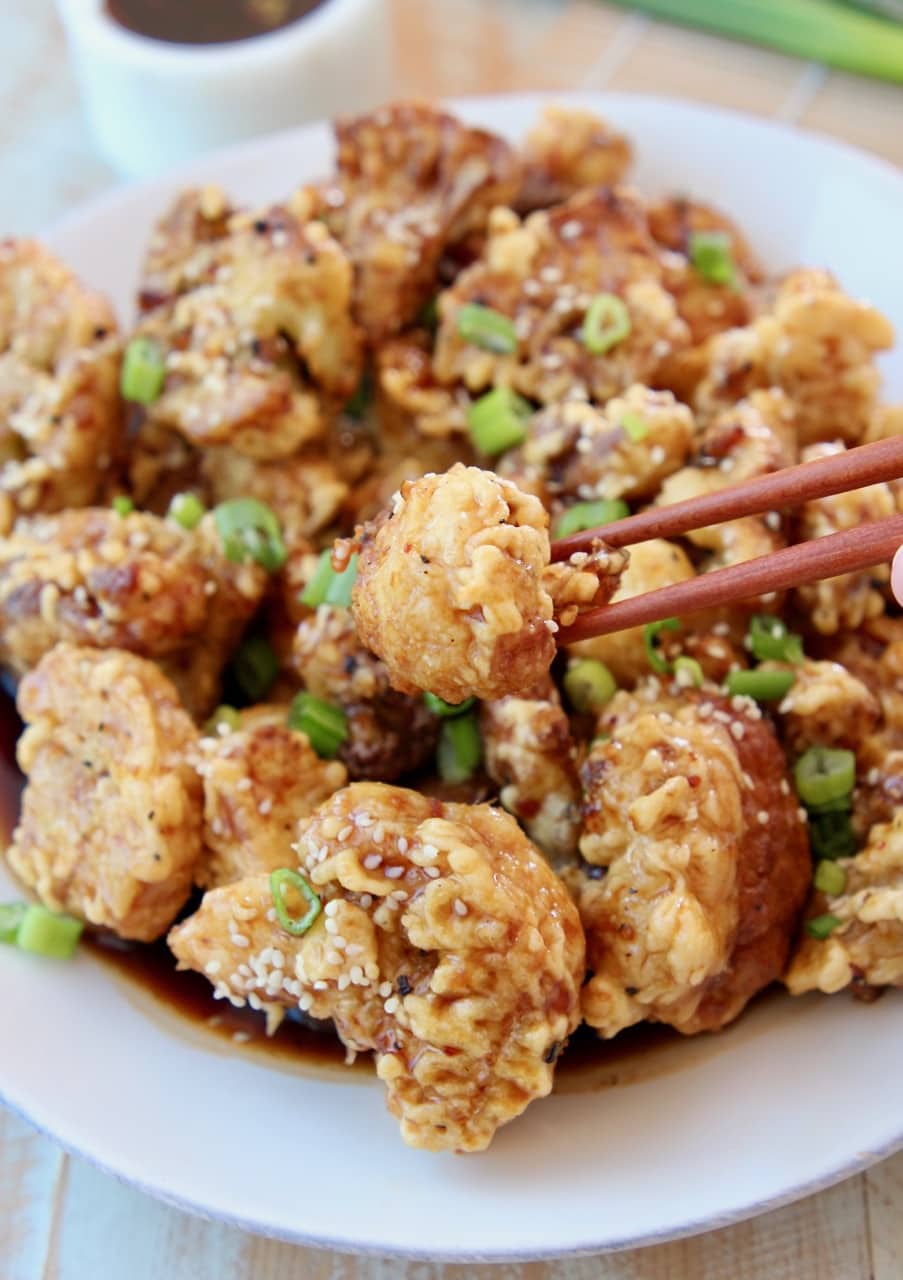 Korean fried cauliflower on plate with chopsticks picking up one piece of cauliflower