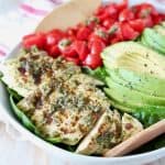 Sliced pesto chicken in bowl with sliced avocado and diced cherry tomatoes