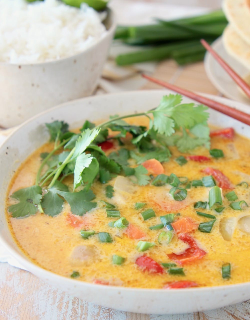 Yellow curry in bowl, topped with fresh cilantro sprigs, with bowl of rice on the side