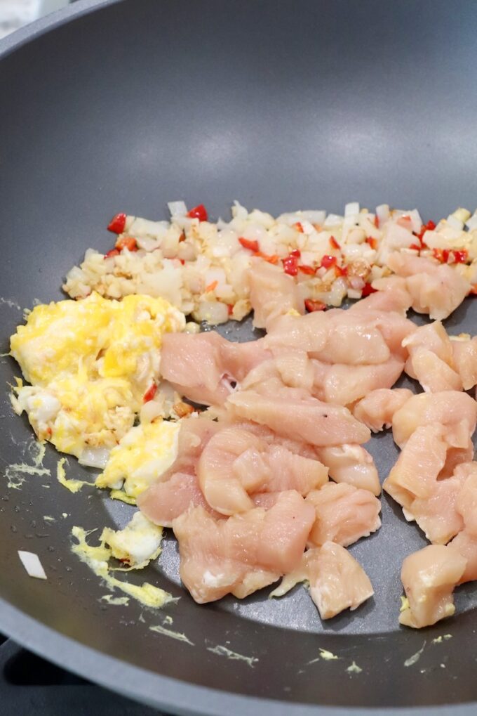 diced raw chicken in large wok with scrambled eggs and diced vegetables