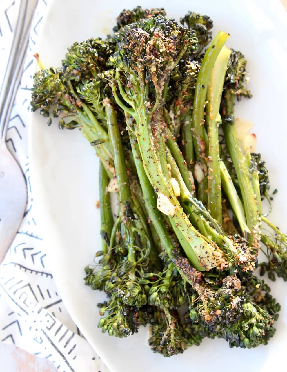 Garlic parmesan broccolini stacked up on top of each other on white plate