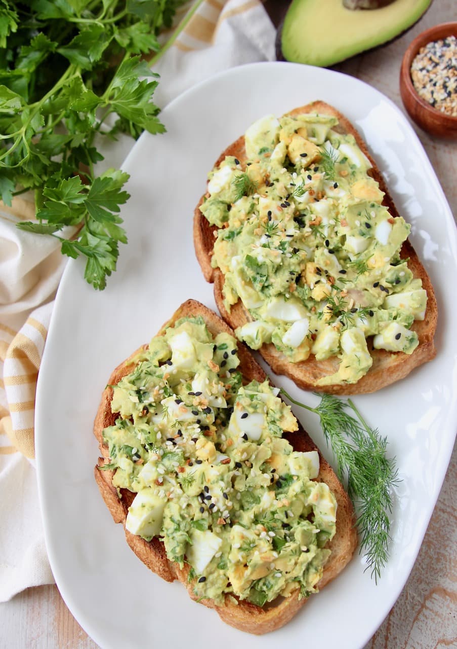 Overhead shot of two pieces of toast, topped with avocado egg salad and fresh dill