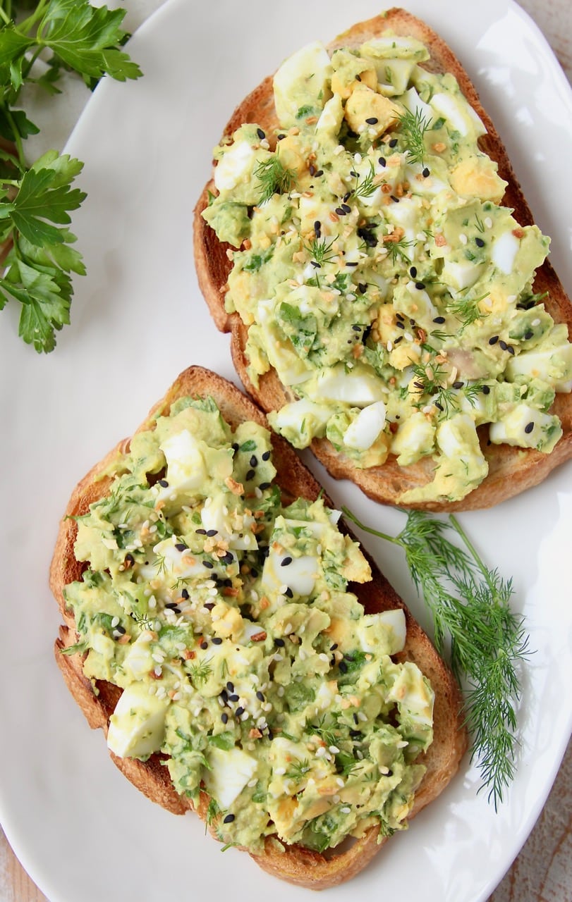 Avocado egg salad on two pieces of toast on a white plate with fresh dill