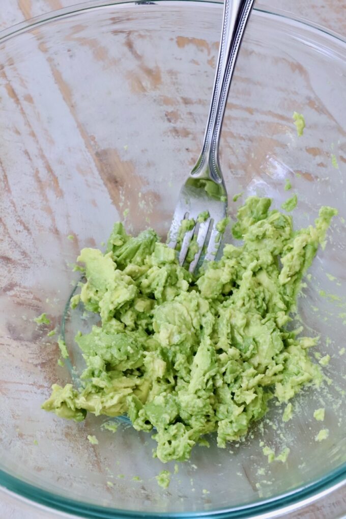 smashed avocado in a glass bowl with a fork