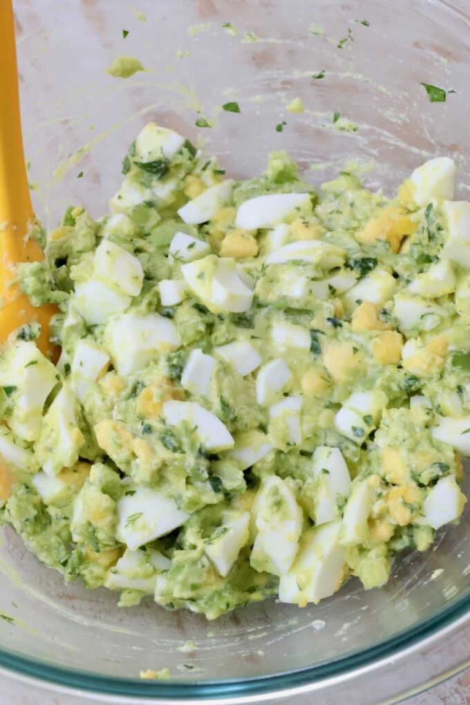 avocado egg salad in a glass bowl with a yellow spatula