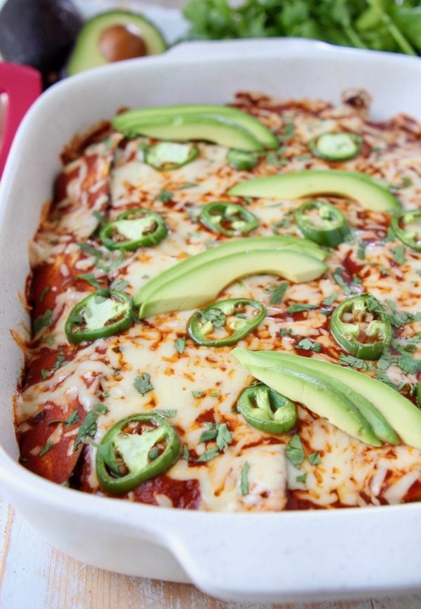 Low carb enchiladas with red sauce in casserole dish topped with sliced jalapenos and avocado