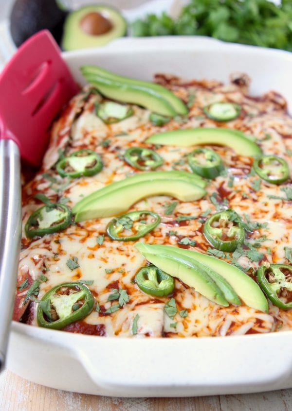 Enchiladas in baking dish with red spatula on the side of the dish