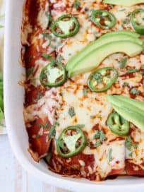 Overhead shot of enchiladas in casserole dish topped with sliced avocado and jalapenos