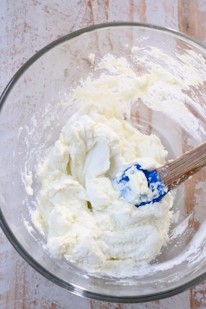 goat cheese whipped in a glass bowl with a blue spatula