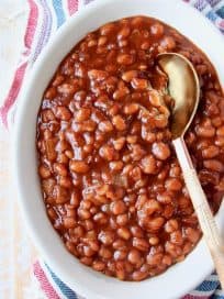 Baked beans in oval bowl with serving spoon in the bowl