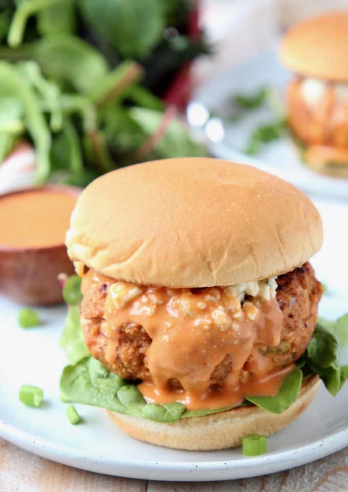 Buffalo chicken burger on bun covered in buffalo sauce sitting on plate