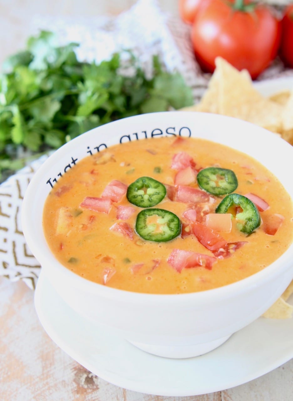 Queso in white bowl topped with diced tomatoes and sliced jalapenos