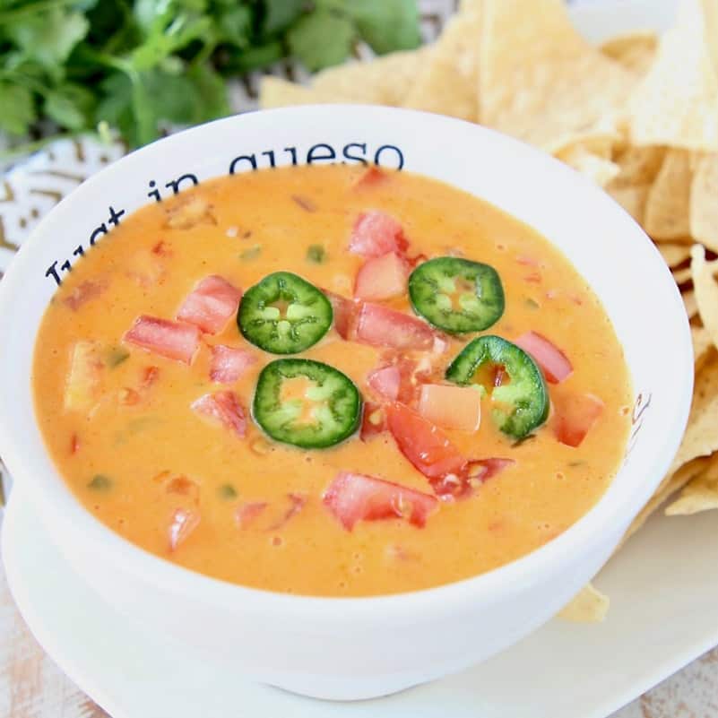 Queso dip in white bowl with tortilla chips on the side