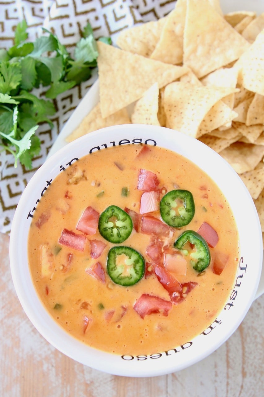 Queso dip in white bowl topped with diced tomatoes and jalapeno slices