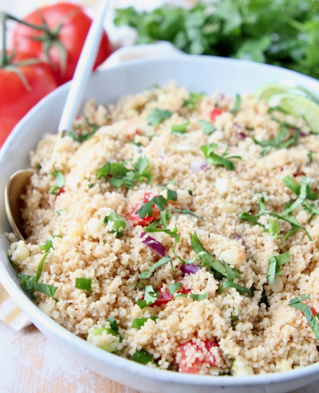 Bowl filled with couscous, diced tomatoes, cilantro and lime wedges