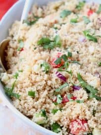 Couscous in bowl with white and gold spoon, topped with chopped cilantro