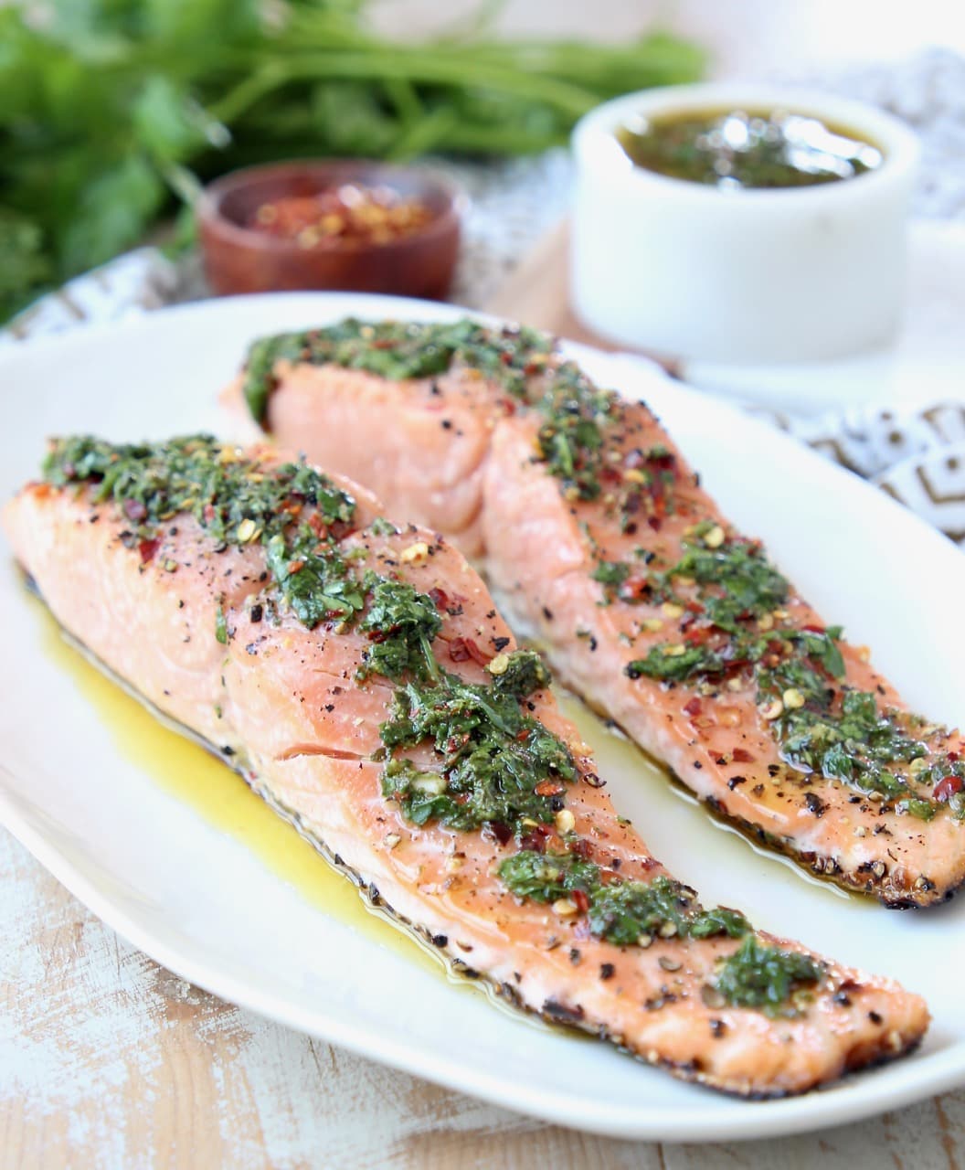 Two filets of grilled salmon on a white plate topped with chimichurri sauce