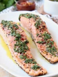 Two pieces of salmon on plate topped with chimichurri sauce