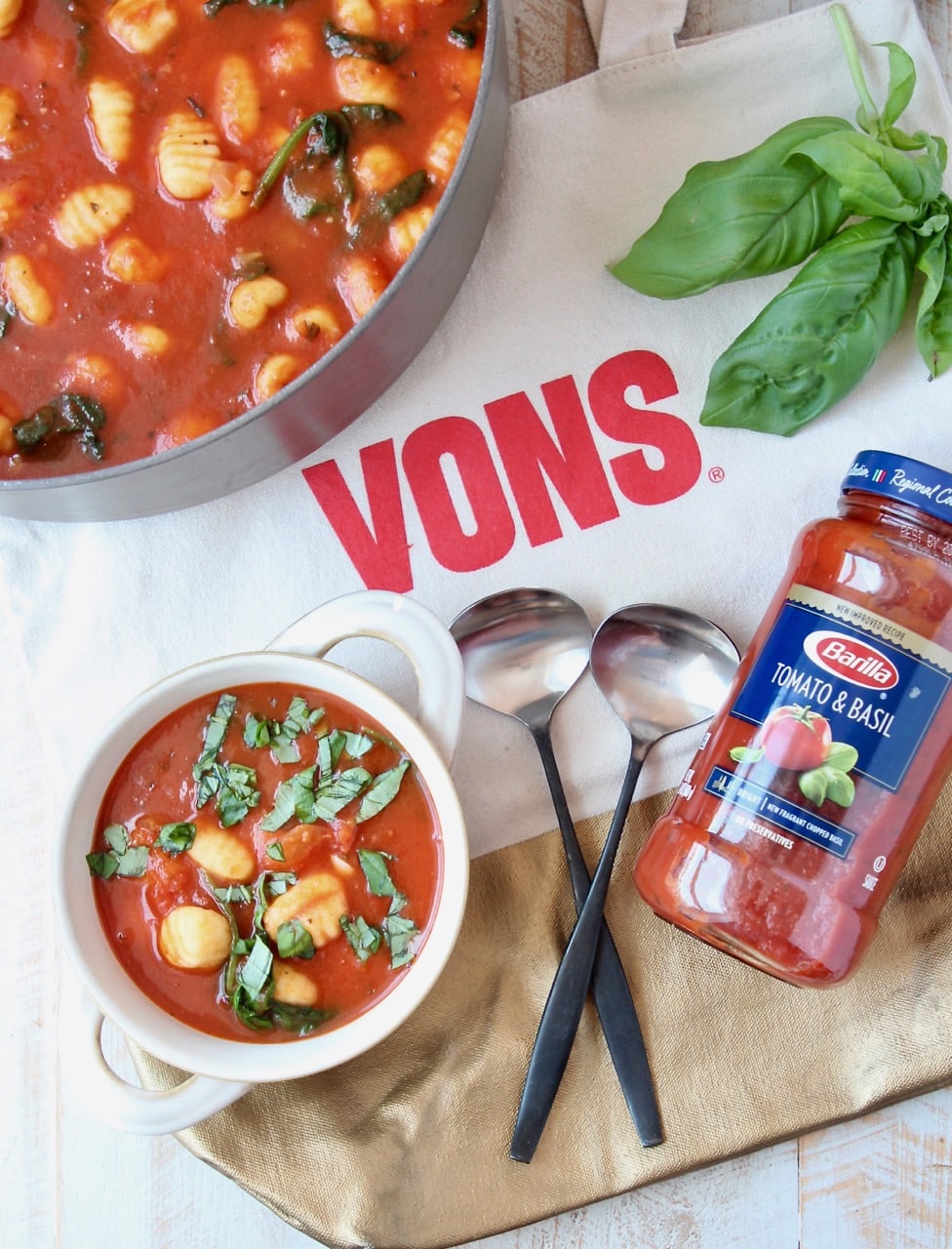 Bowl of soup, sitting on Vons bag with two spoons and jar of tomato sauce