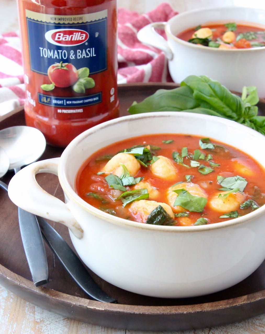 Gnocchi soup in white crock on wood serving tray with spoons