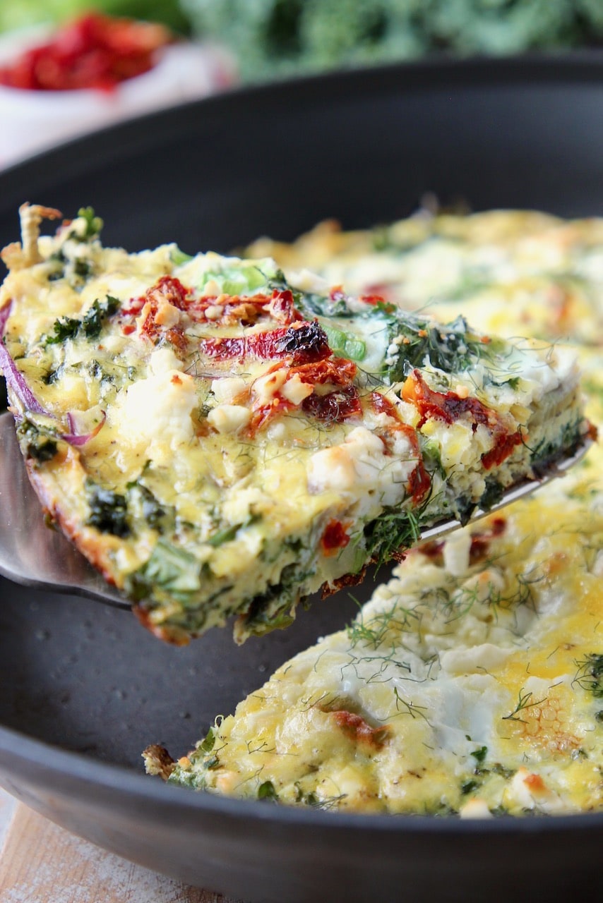 Slice of vegetable frittata lifted out of skillet with a spatula