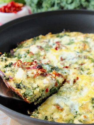 Slice of vegetable frittata being lifted out of skillet with silver spatula