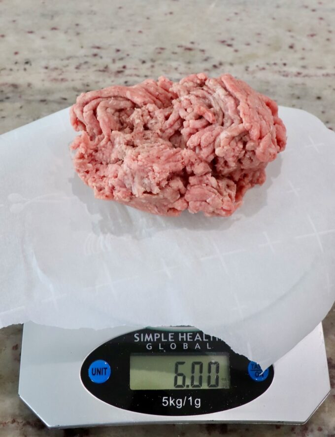 ground beef on a piece of parchment paper on a kitchen scale