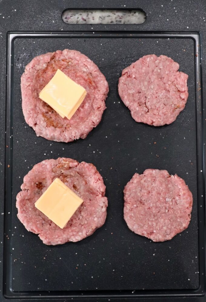 ground beef patties stuffed with cheese slices on a cutting board
