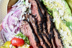 Grilled steak salad in bowl with avocado slices and sliced onions