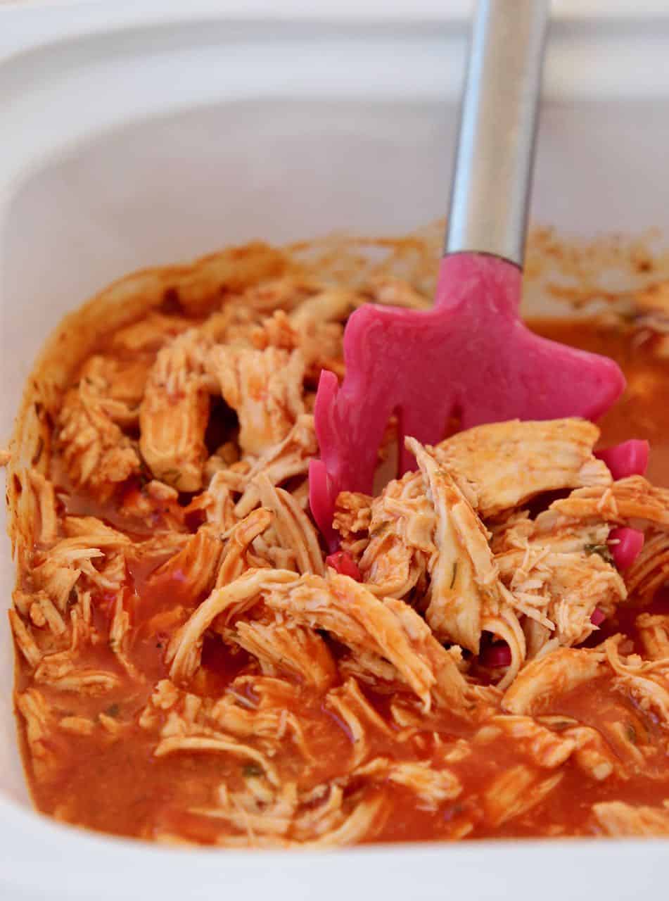 Shredded buffalo chicken in crock pot with red slotted serving spoon