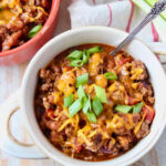 chili in a bowl topped with melted shredded cheese and diced green onions