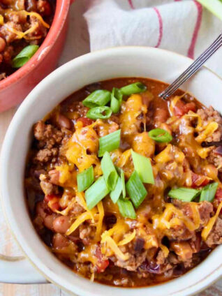 chili in a bowl topped with melted shredded cheese and diced green onions